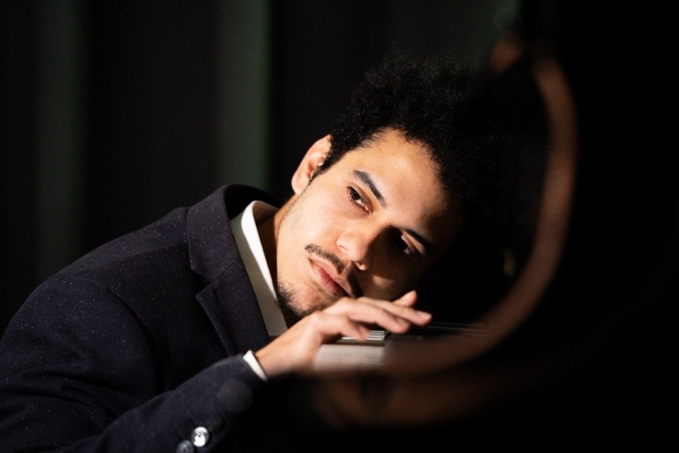 Manuel Sanguino resting his head on the piano, one hand on the keys